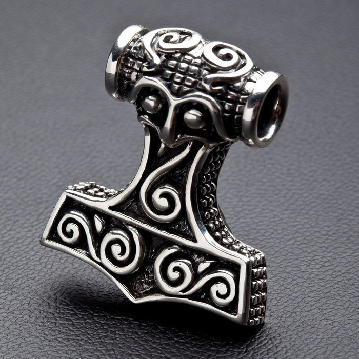 Angled close-up revealing the intricate swirling Norse engravings and darkened textured edges of the solid silver hammer.