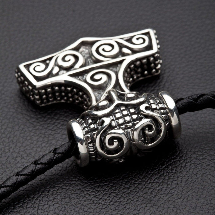 Beaded side thickness and swirling silver bail of the heavy Mjolnir pendant threaded on a black braided cord.