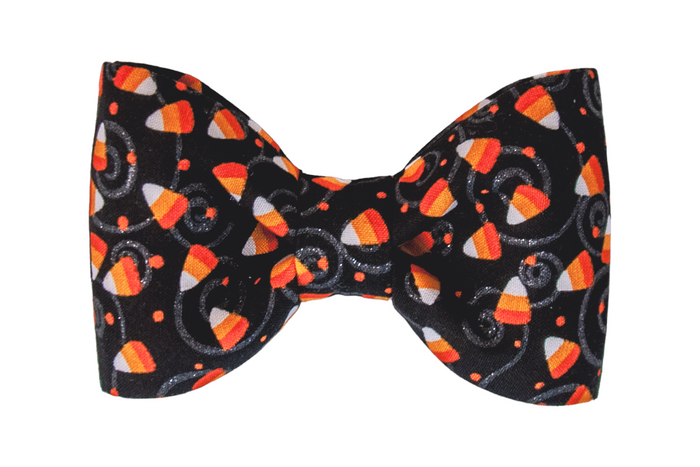 Halloween bow tie for dogs featuring a black fabric patterned with bright candy corn pieces. The design is accented with playful swirls and tiny dots, creating a fun, seasonal accessory for fall celebrations.