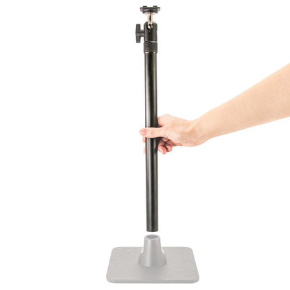 A hand holds a vertical black pole above a gray square base from the TW Broadcaster Live Streaming Extension Kit with 29-inch Pole and Dual-T Head, preparing to insert it—ideal for dual phone or live streaming setups.